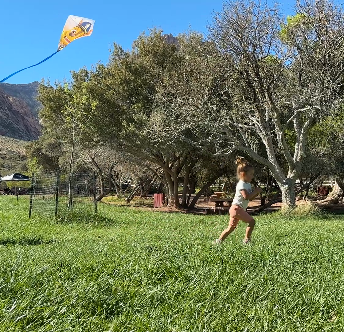 A child flying a kite in a park, with "Her First Kite!" handwritten in yellow